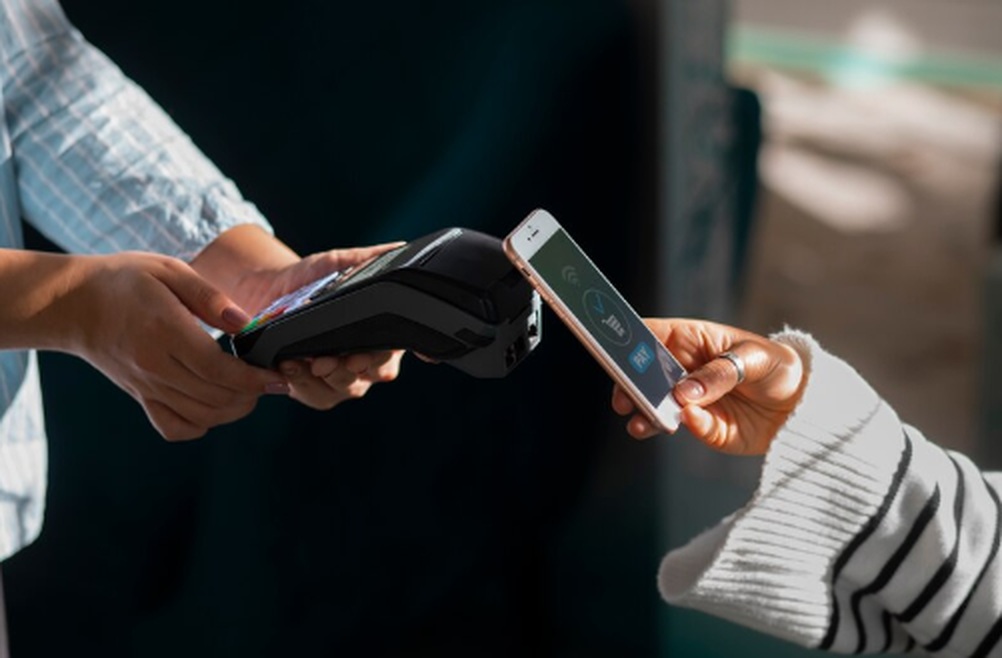Person making an instant pay transaction using a smartphone and contactless payment terminal, illustrating modern digital salary access.