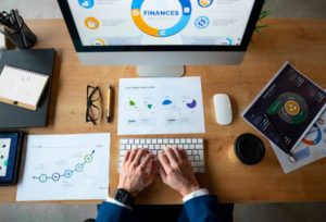 Business professional analyzing financial charts and digital dashboards on a computer and printed reports, illustrating data-driven strategies in the Open Finance ecosystem.