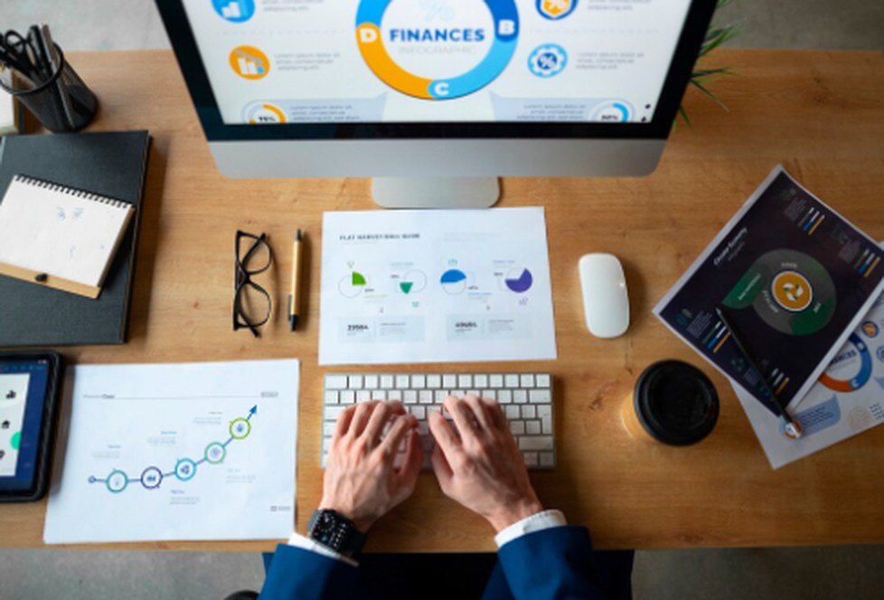 Business professional analyzing financial charts and digital dashboards on a computer and printed reports, illustrating data-driven strategies in the Open Finance ecosystem.