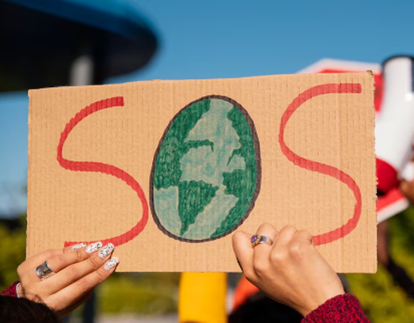 Hands holding a cardboard sign with the word "SOS" and a drawing of Earth, symbolizing a call for action during the climate crisis.