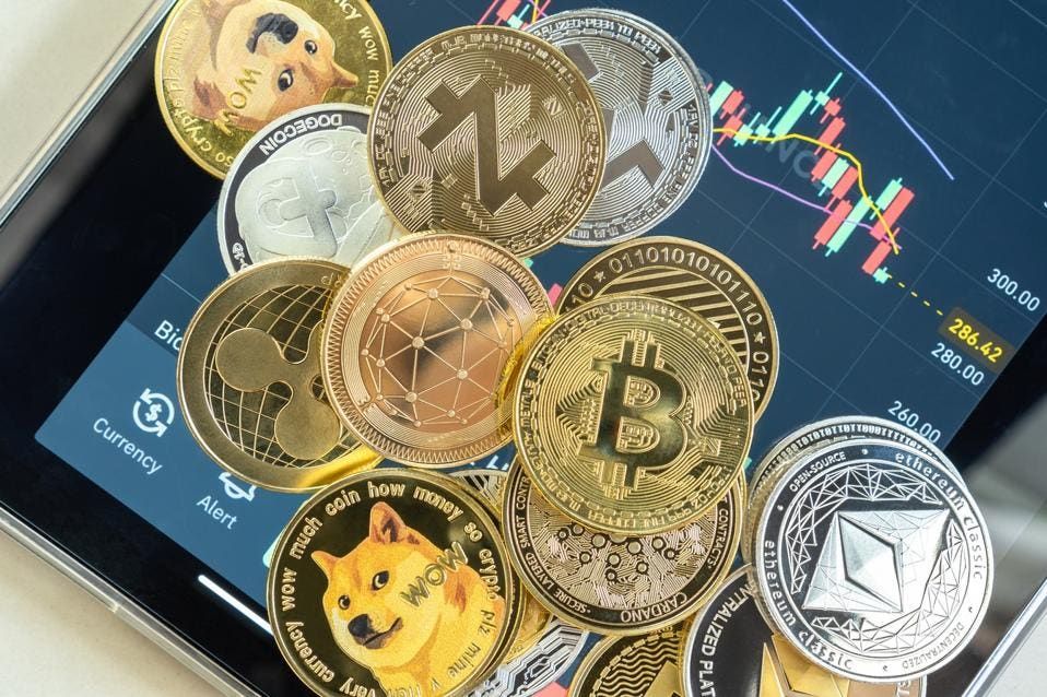 A collection of various coins representing digital currencies, such as Bitcoin, Ethereum, Ripple, and Dogecoin, placed on top of a smartphone screen displaying financial charts and market data.